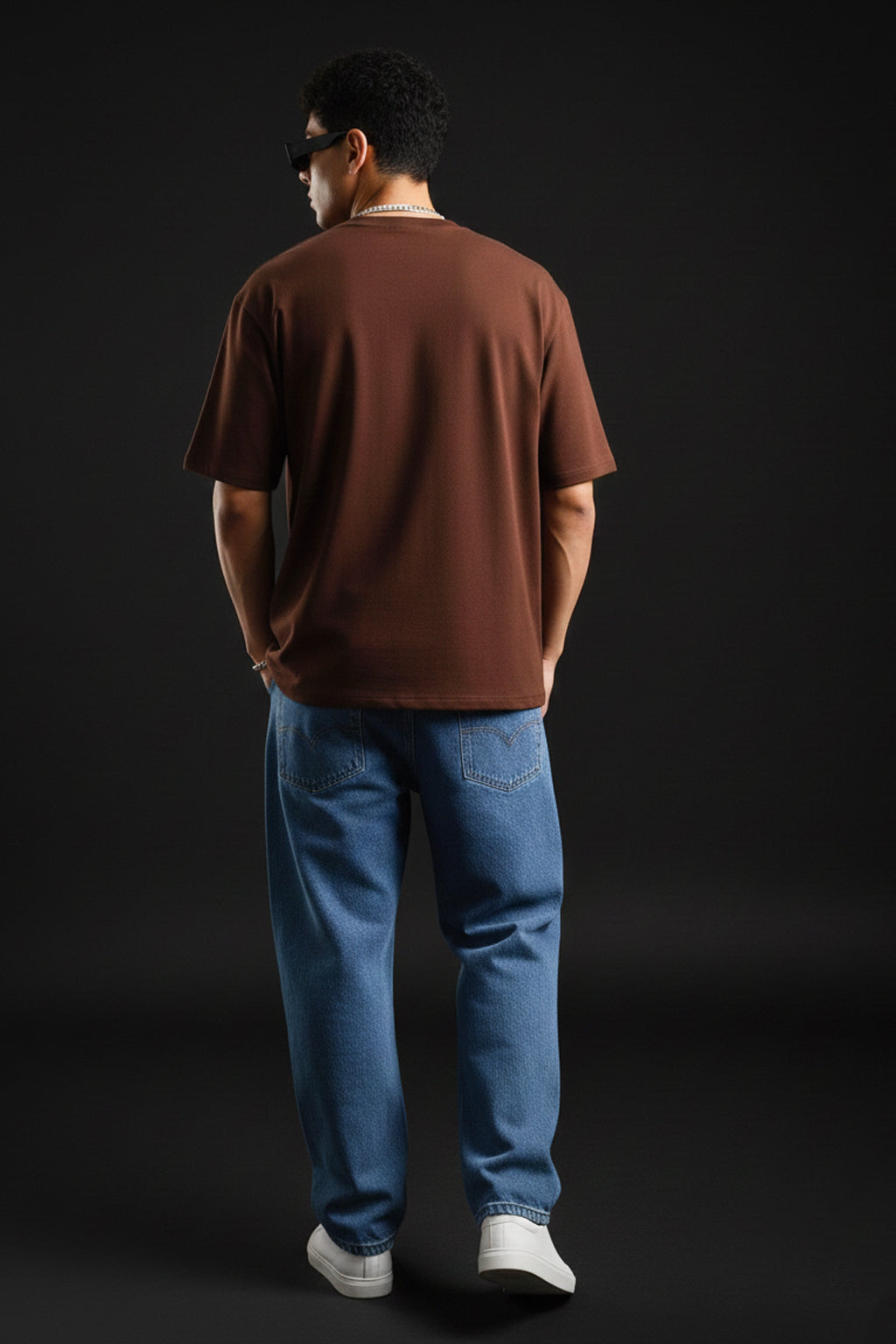 Person wearing a brown shirt and blue jeans standing against a black background