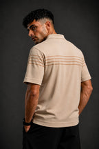 A man wearing a beige short-sleeve polo shirt with thin horizontal brown stripes across the upper back, shown from a three-quarters back view against a dark gray studio background.