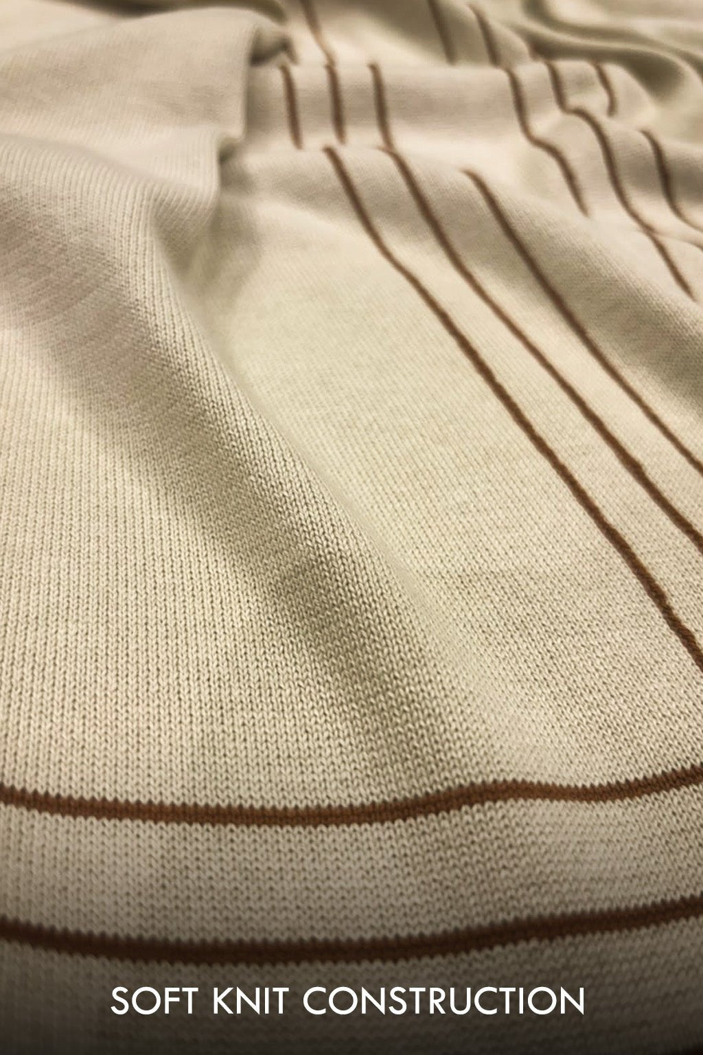 Close-up of a cream-colored knit fabric with thin brown stripes, showing the soft knit texture and construction. White text at the bottom reads 'SOFT KNIT CONSTRUCTION'.