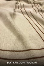 Close-up of a cream-colored knit fabric with thin brown stripes, showing the soft knit texture and construction. White text at the bottom reads 'SOFT KNIT CONSTRUCTION'.