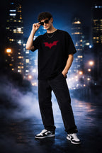 Person wearing a black t-shirt with a red bat logo against a cityscape background