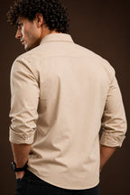A man wearing a light beige long-sleeve button-down shirt, shown from the back against a dark brown studio background.