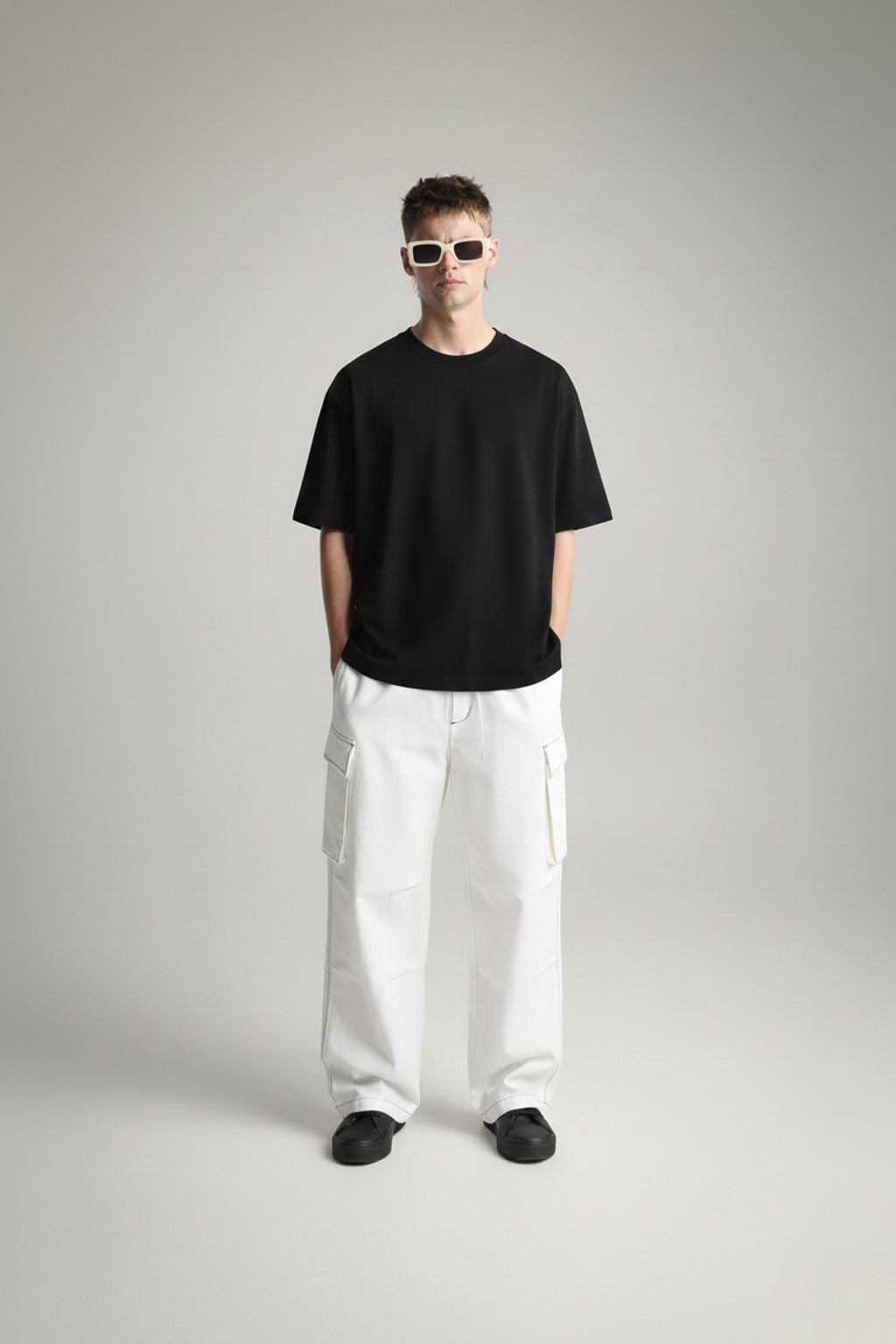Person wearing a basic black t-shirt and white pants on a gray background
