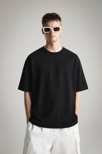 Person wearing a plain oversized black t-shirt and white pants with sunglasses on a gray background