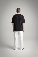 Person wearing a black t-shirt and white pants on a gray background back pose