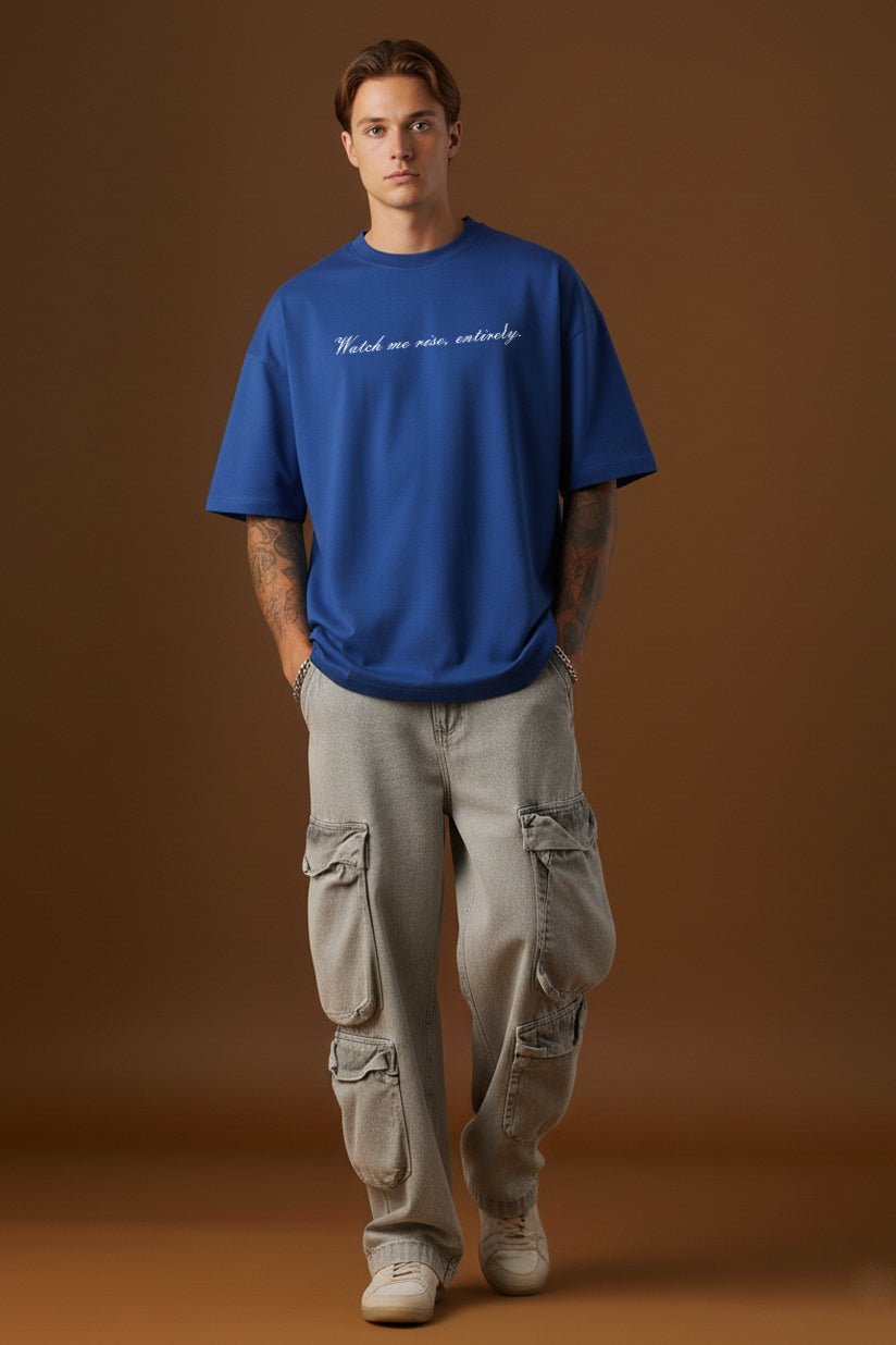 Male model wearing blue oversized t-shirt with Watch me rise entirely quote front print full body view