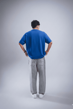 Person wearing a blue shirt and gray pants standing against a plain background