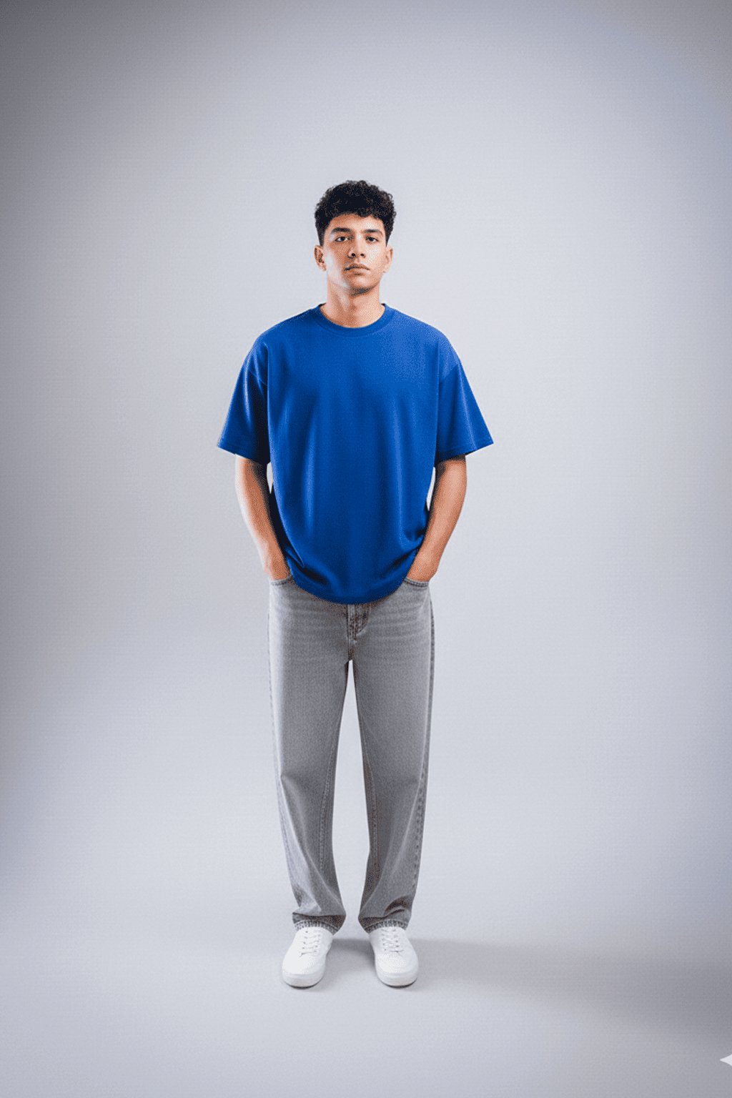 Person wearing a blue t-shirt and gray pants on a plain background with hands in pocket