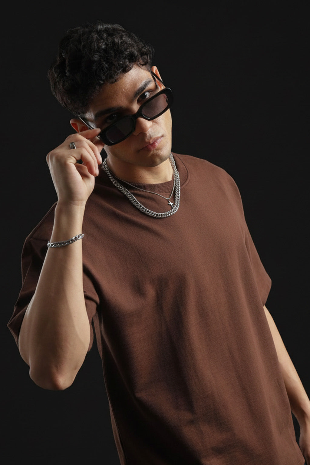 Man wearing sunglasses and a brown tshirt against a black background