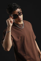 Man wearing sunglasses and a brown tshirt against a black background