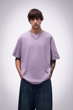 Person wearing a lavender oversized purple t-shirt and dark jeans on a plain background