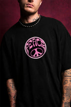 Person wearing a black t-shirt with a pink 'PEACE' symbol design on a dark background