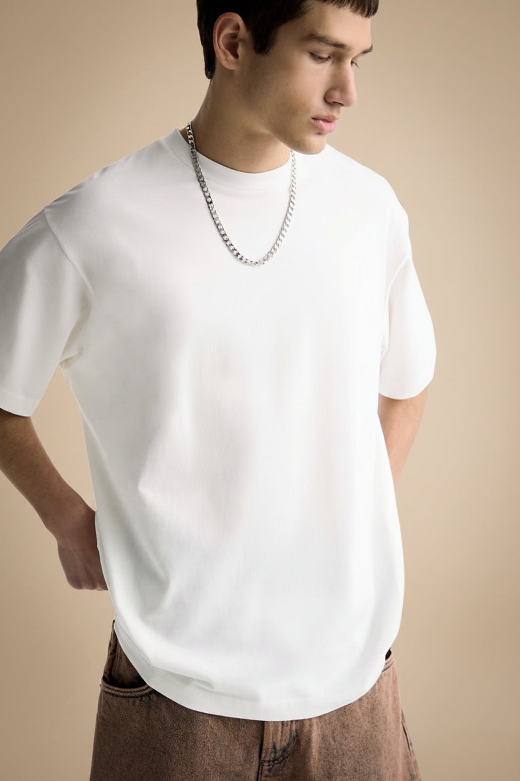 Man wearing a plain white oversized t-shirt and brown pants on a beige background