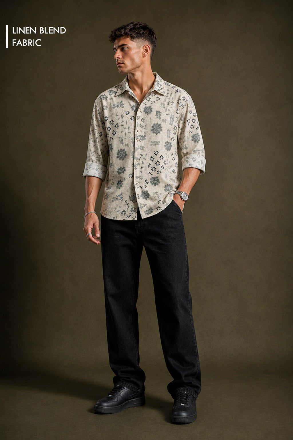 A man modeling a light beige linen-blend button-up shirt with a dark gray floral pattern, paired with black trousers and black shoes, against a dark olive-brown studio background. The text 'LINEN BLEND FABRIC' is visible in the top-left corner.